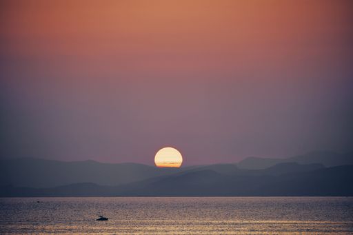 A beautiful shot of the sea with the sun going down behind the mountains at sunset