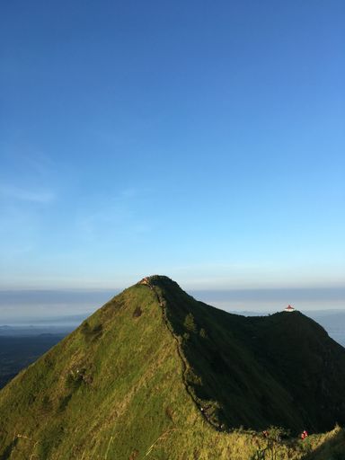 A vertical shot of a green hill with a hiking road against blue sky background