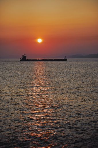 A vertical shot of a boat sailing in the sea in the distance under a beautiful sky at sunset