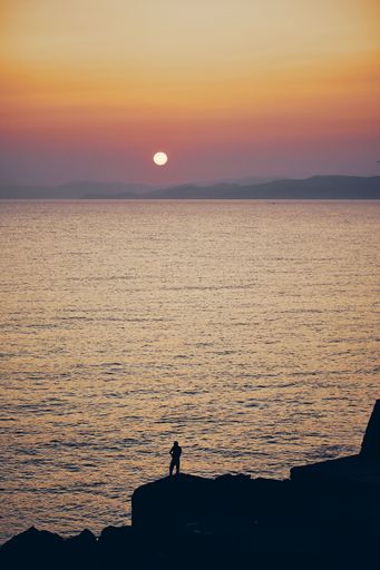 A silhouette of a person on a cliff near the sea with a beautiful sky in the background at sunset in a vertical shot