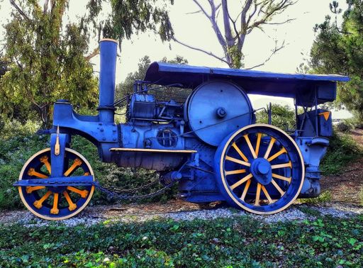 A blue vehicle with a steam engine near trees with a bright sky in the background in Trragones