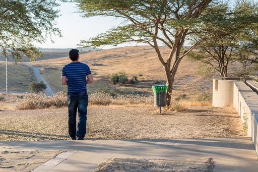 A Caucasian man standing in the park near the waste bin