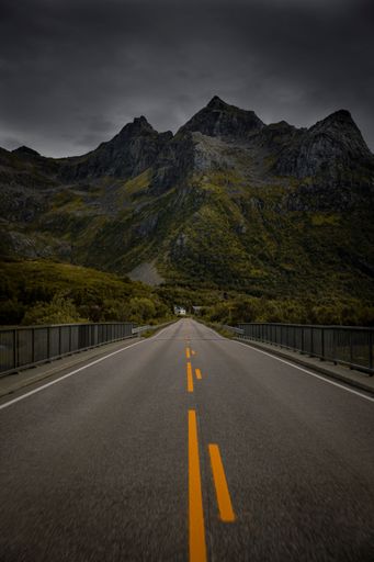 A vertical shot of an asphalt road with rocky mountains in the background in a rural area