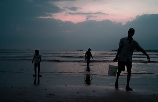 The silhouettes of the people on the shore against the cloudy sky at sunset.