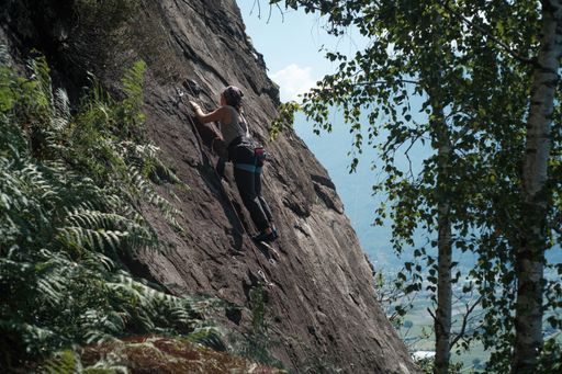 The young female climber on the rocky slope surrounded by green vegetation.