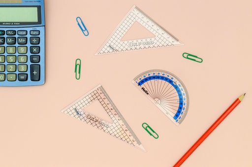 A top view of rules, a calculator, and other school supplies on a pink surface