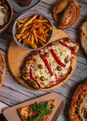 A vertical top view of a Neapolitan pizza with olives and a bowl of french fries