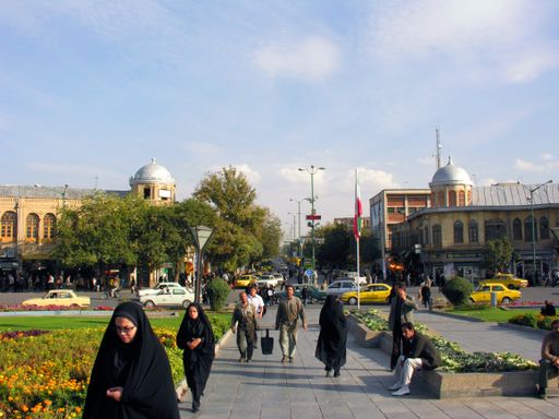 People walking through Imam Khomeini Square, Hamadan, Iran. The image shows also lawns and flowerbeds in the square and a few of the city's buildings