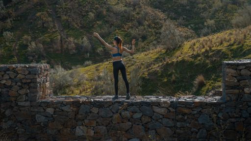 A female standing on a stone wall doing a workout with beautiful nature in the background