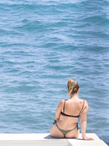 A sexy woman with swimsuit sitting on the white surface in front of the sea