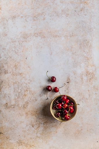 A vertical image of red ripe cherries in a bowl on a concrete surface with space for your text