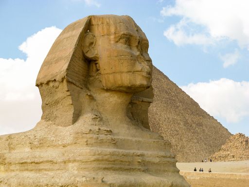 A closeup shot of the body of Sphinx in desert with the Great Pyramid of Giza in the background