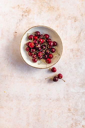 A vertical image of red ripe cherries in a bowl on a concrete surface with space for your text