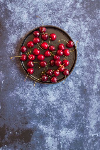 A vertical image of red ripe cherries on saucer on a concrete surface with space for your text