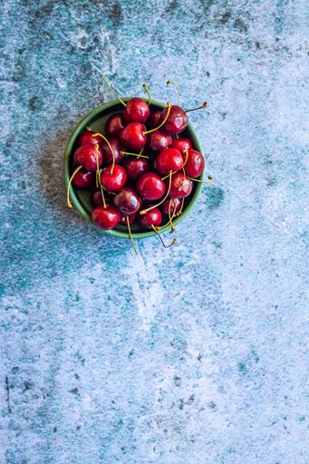 A vertical image of red ripe cherries in a bowl on a concrete surface with space for your text