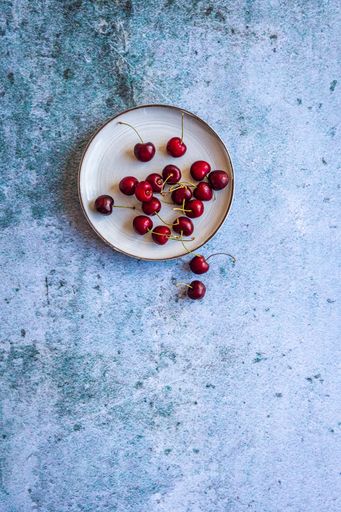 A vertical image of red ripe cherries on a saucer on a concrete surface with space for your text