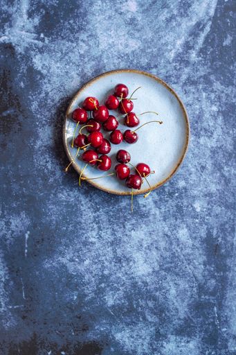 A vertical image of red ripe cherries on a saucer on a concrete surface with space for your text