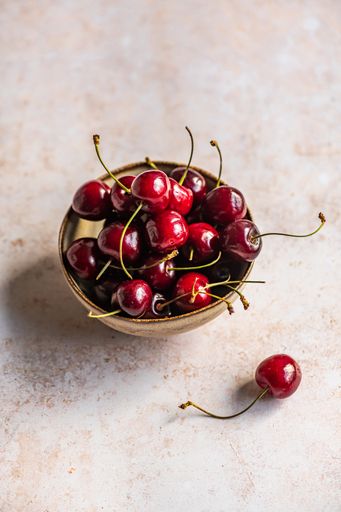 A vertical image of red ripe cherries in a bowl on a concrete surface