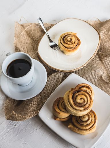 A vertical shot of cinnamon rolls stacked on top of each other on the plate with a cup of coffe