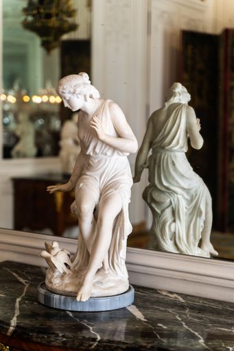 A vertical shot of a small female sculpture near a reflective mirror in the Versailles, Palace