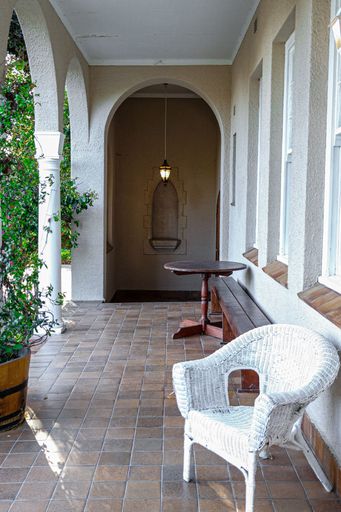 A vertical shot of an elegant front yard patio with a seat, a table and a lamp hanging from an archway