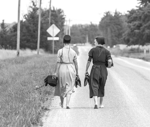 A vertical grayscale shot of two Amish women walking down road.