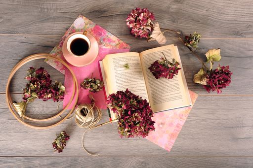 An overhead shot of a cup of coffee with faded roses and an open book on a wooden background