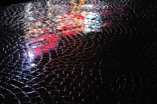 A closeup of reflections of neon lights on a wet rainy street of cobblestone at night