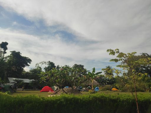 A scenic view of colorful tents in a forest surrounded by wild nature in cloudy sky background