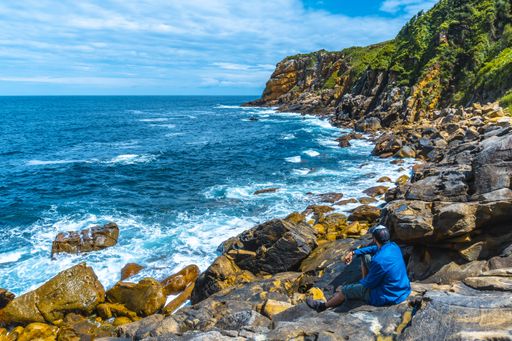 A high angle shot of a male sitting on the shore and looking to the beautiful boundless sea waves