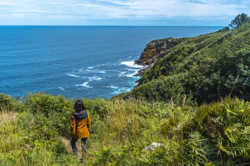 A high angle shot of a female standing on the field and looking to the beautiful boundless sea