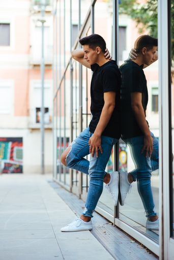 A young attractive man with black T-shirt and ripped jeans leaning to the glassy wall