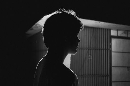 A grayscale shot of a South Asian boy standing against a lightbulb