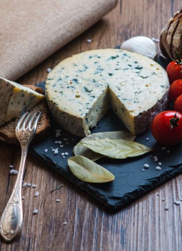 A vertical shot of a Roquefort cheese next to tomatoes and fork