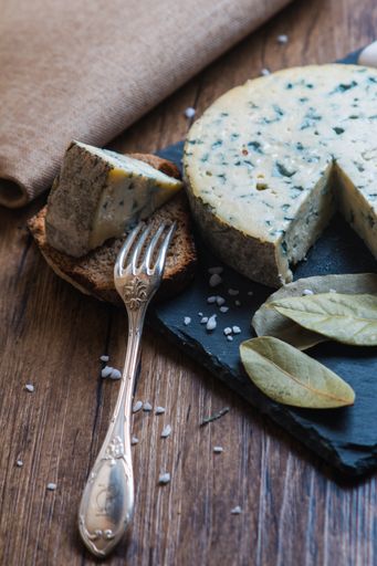 A vertical shot of blue cheese next to bread, fork, and bay leaves