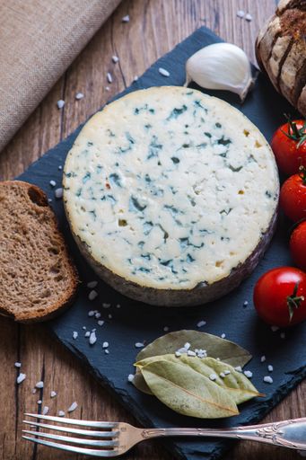 A vertical shot of the blue cheese next to fork,  tomatoes, garlic, bread and bay leaf