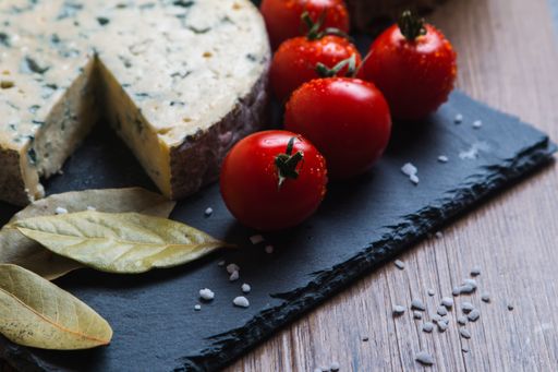 A closeup shot of blue cheese next to tomatoes and bay leaf
