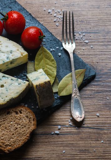 A vertical shot of bay leaves, fork, tomatoes and bread next to blue cheese