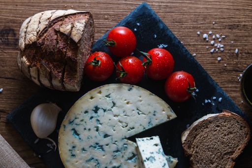 A round blue cheese surrounded by bread, tomatoes and garlic