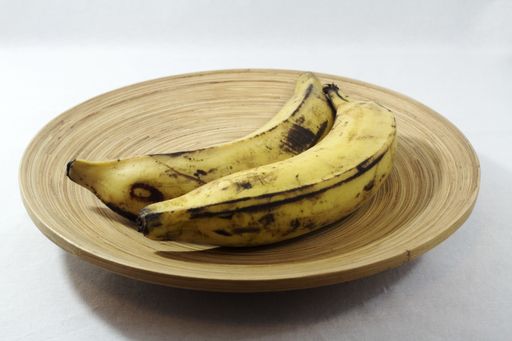 The two ripe bananas served in a wooden plate isolated on the white background