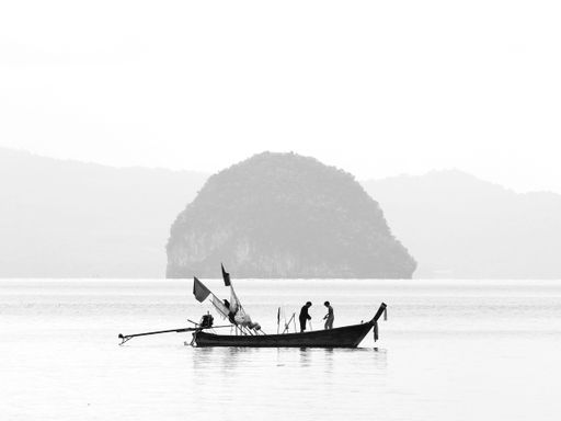 A grayscale of a couple of fishermen standing on boat in the ocean