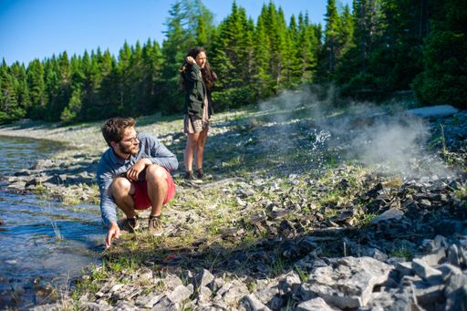 Anticosti Island, Quebec / Canada - July 14 2018: Young Woman with Long Hair and Young Caucasian Adult Male are Looking at the Campfire in a Shore
