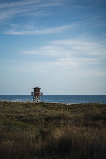 A beautiful view of a green field with a lifeguard tower at the sea coast against a cloudy sky