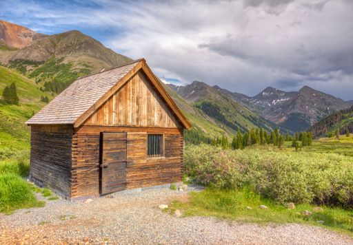 A scenic shot of a small wooden house in a rural area surrounded by scenic landscape and greenery