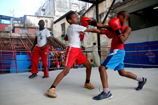 A trainer teaching two afro American young males to fight in a boxing club. Better start at a young age