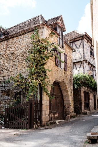 A vertical shot of an old brick french house with a creeping plant plant and arched windows