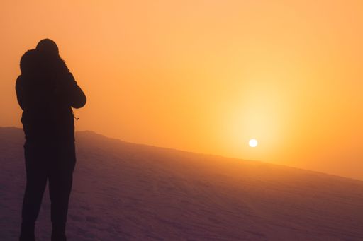 A beautiful view of a hiker on a snowy hill with fog during sunset