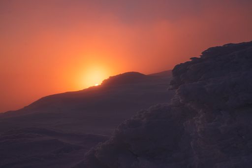A beautiful view of a snowy hill during orange sunset