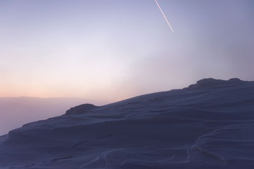 A beautiful view of a snowy hill with fog during sunset