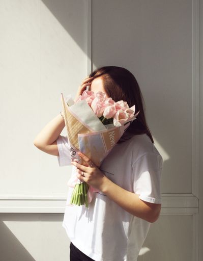 A vertical shot of a female covering her face with a pink tulip bouquet near a sunny window